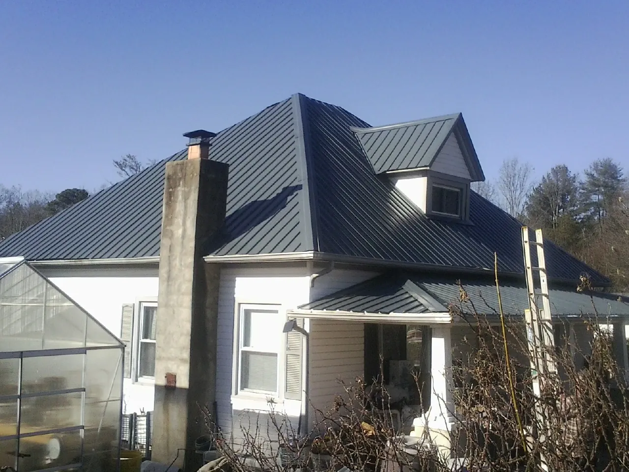 Dark blue standing seam metal roof on a white farmhouse with dormer — Slate & Tile Roof Repair by Roofing Brothers in Overland Park