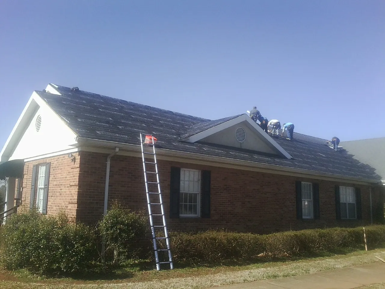 Crew tearing shingles off a brick ranch roof with a ladder set — Emergency Roof Repair work by our crew in Overland Park