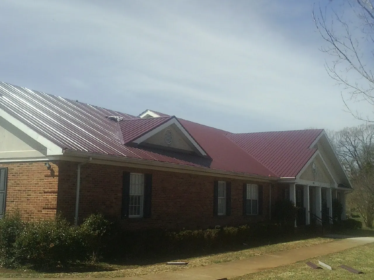 Red metal roof with gabled entries on a long brick building, from a Hail Damage Roof Repair job in Overland Park