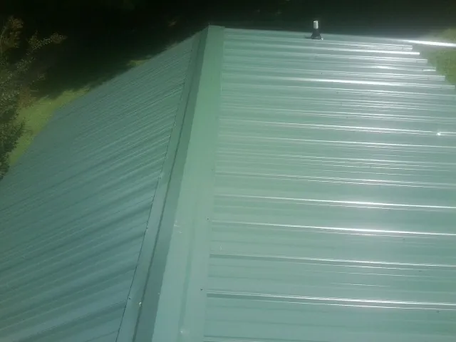 New green metal panels meeting at the ridge of a roof — Flat Roof Repair work by our crew in Overland Park