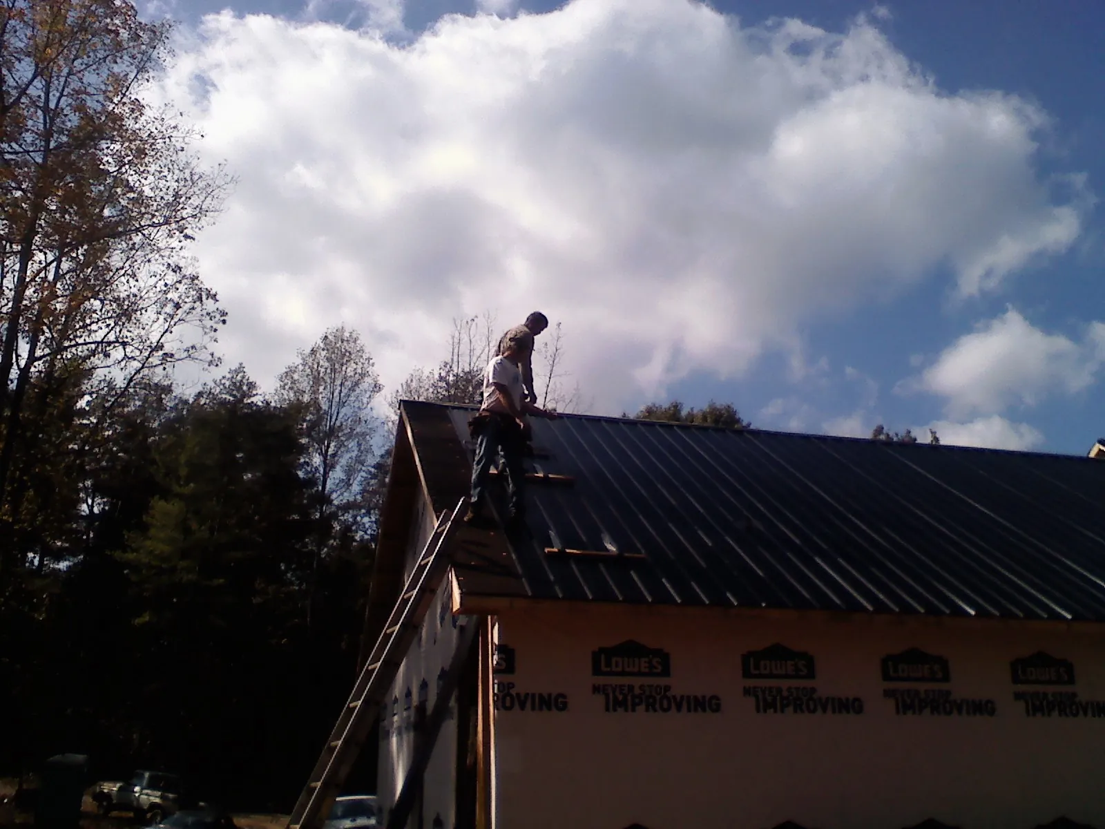 Roofer fastening dark metal panels high against a cloudy sky, from a Roof Inspection job in Overland Park
