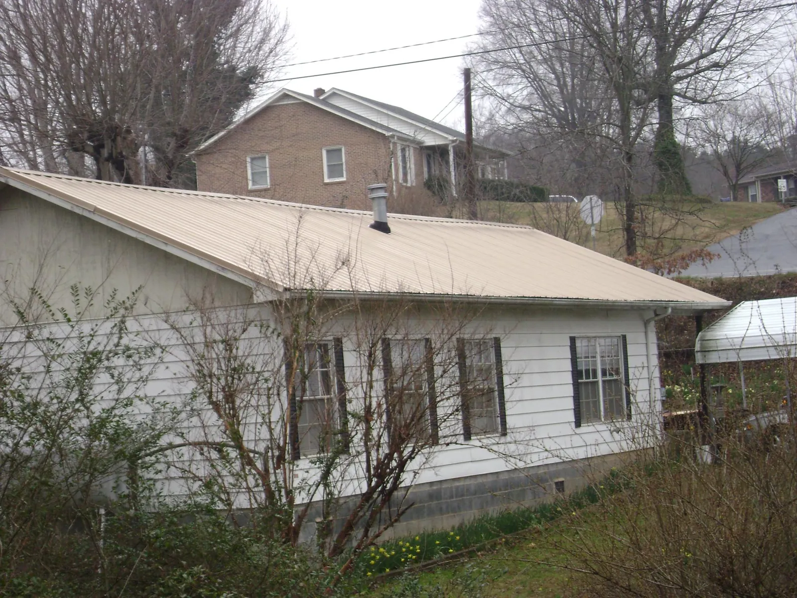 Tan metal roof on a white sided house set into a hillside — Commercial Roofing by Roofing Brothers in Overland Park